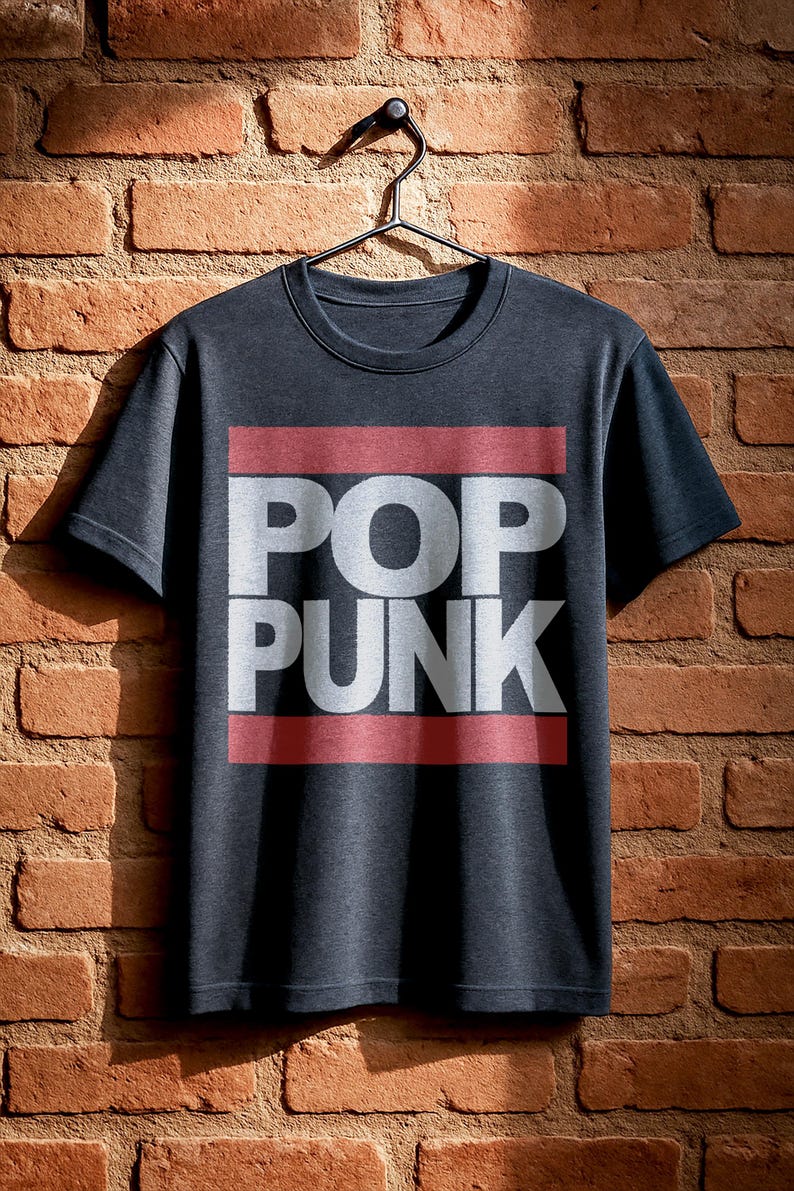 May include: Dark gray t-shirt with the words "POP PUNK" in white block letters, set against a red rectangular background. The shirt is hanging on a black hanger against a brick wall.