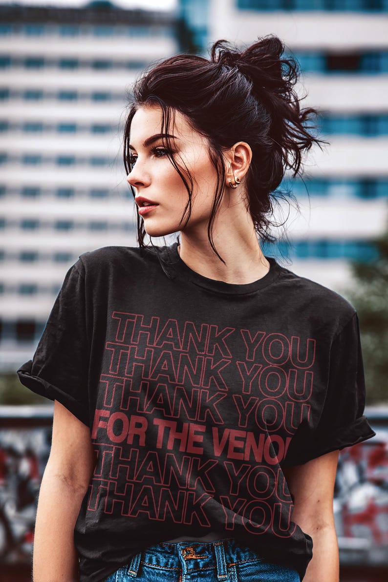Pu&ograve; includere: T-shirt nera con la scritta "THANK YOU" ripetuta pi&ugrave; volte in rosso. Anche la frase "FOR THE VENOM" &egrave; in rosso. La maglietta &egrave; indossata con jeans blu.