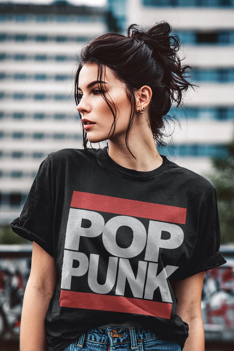 May include: Black t-shirt with the words "POP PUNK" in large white letters, set against a red stripe. The shirt is worn by a person with dark hair and is paired with blue jeans.