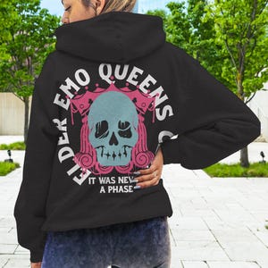 Pu&ograve; includere: Felpa nera con una stampa grafica rosa e bianca di uno scheletro con una corona e il testo "Elder Emo Queens Club" e "It was never a phase".