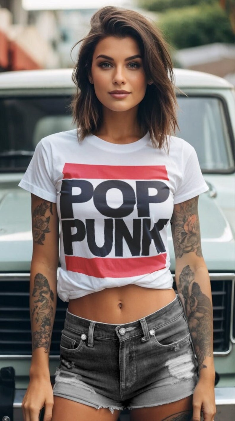 May include: White t-shirt with the words "POP PUNK" in black block letters, framed by red and white stripes. The person is wearing gray denim shorts. The person has tattoos on both arms.