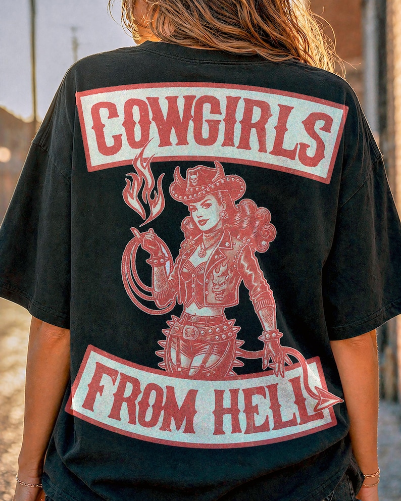 May include: Black t-shirt with a red graphic of a cowgirl holding a lasso and a flame. The text "COWGIRLS FROM HELL" is printed in red on the front and back of the shirt. The shirt has short sleeves.