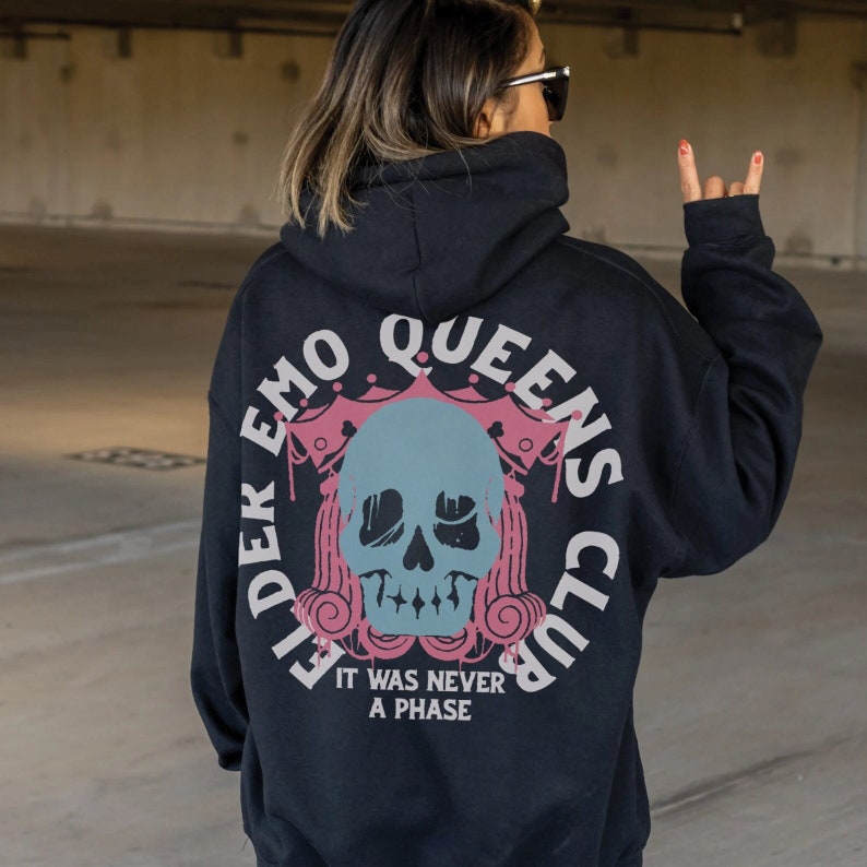 Pu&ograve; includere: Felpa con cappuccio nera con una stampa grafica di un teschio con una corona e il testo "Elder Emo Queens Club" e "It was never a phase".
