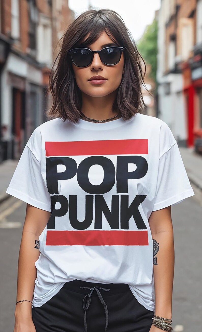 May include: A white t-shirt with the words "POP PUNK" in large black letters, framed by red stripes. The person is wearing black sunglasses and a necklace. The background is a blurred street scene.