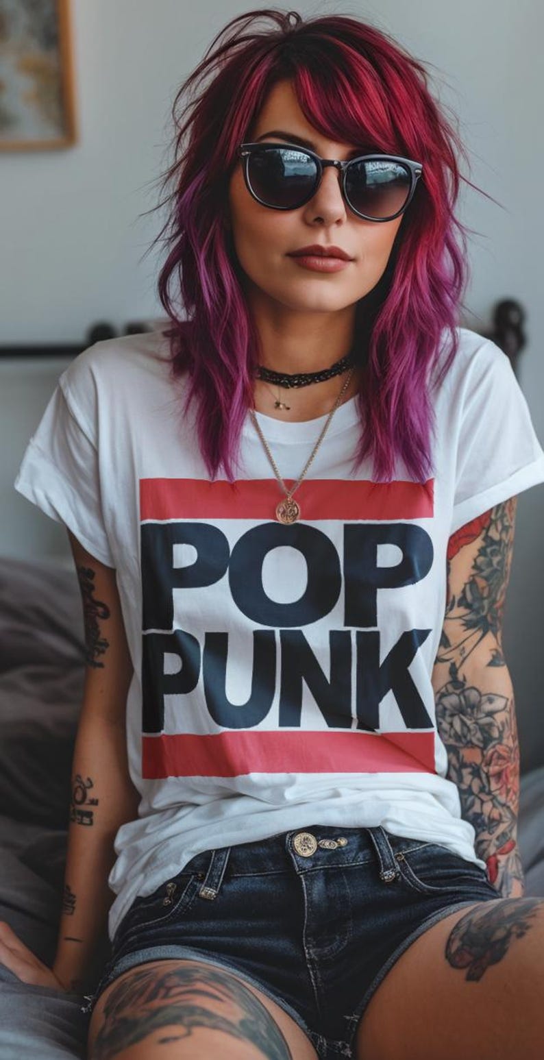 May include: A person wearing a white t-shirt with the words "POP PUNK" in large black letters, set against a red and blue stripe. The person has vibrant purple hair, sunglasses, and tattoos on their arms.