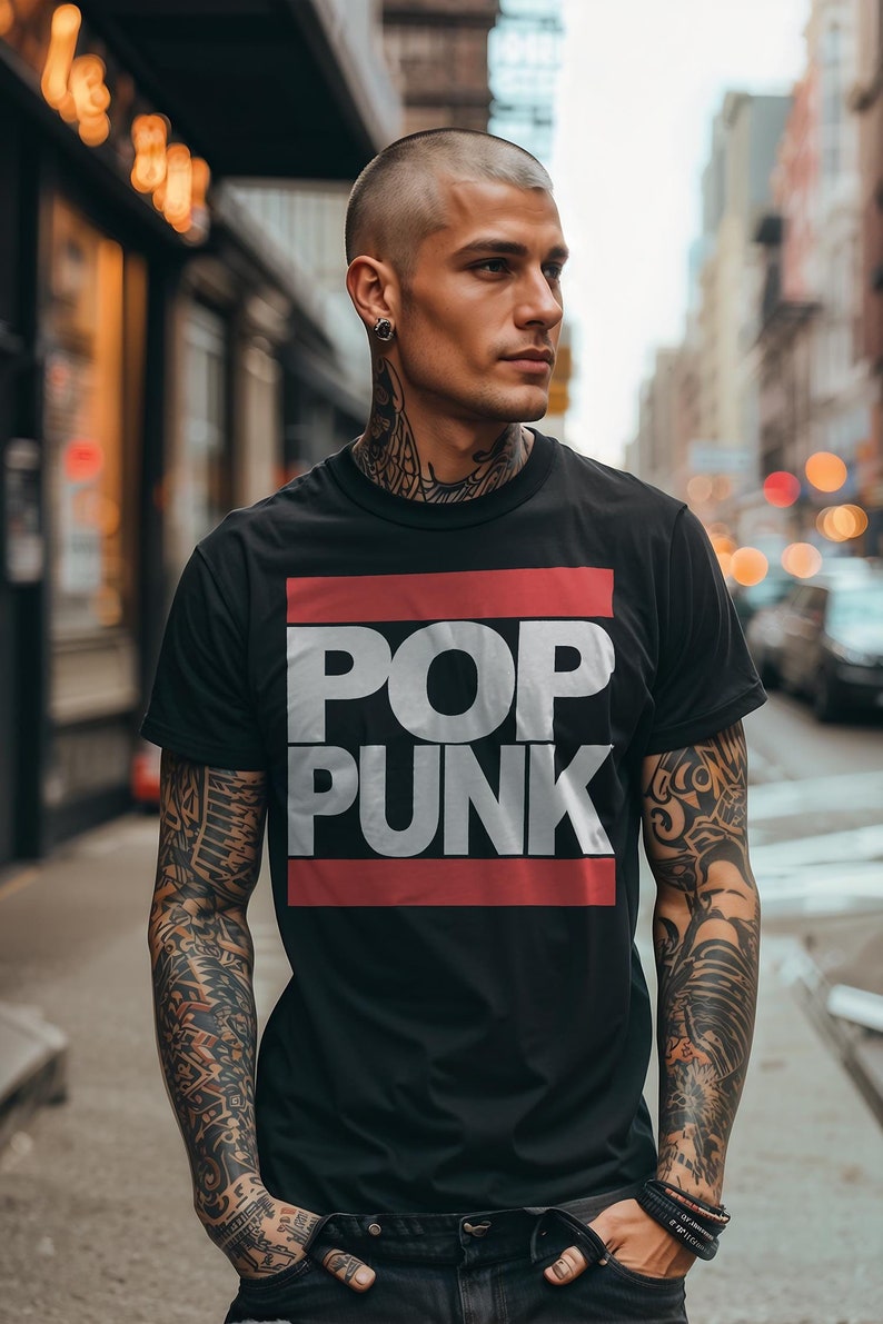 May include: Black t-shirt with the words "POP PUNK" in large white letters, set against a red and white rectangular background. The shirt is short-sleeved and worn by a person with tattoos.