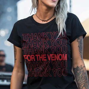 Pu&ograve; includere: T-shirt nero con la scritta rossa "THANK YOU FOR THE VENOM". La maglietta &egrave; indossata da una persona con tatuaggi e occhiali da sole.