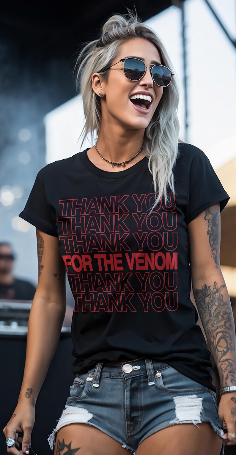 Pu&ograve; includere: T-shirt nero con la scritta rossa "THANK YOU FOR THE VENOM". La maglietta &egrave; indossata da una persona con tatuaggi e occhiali da sole.