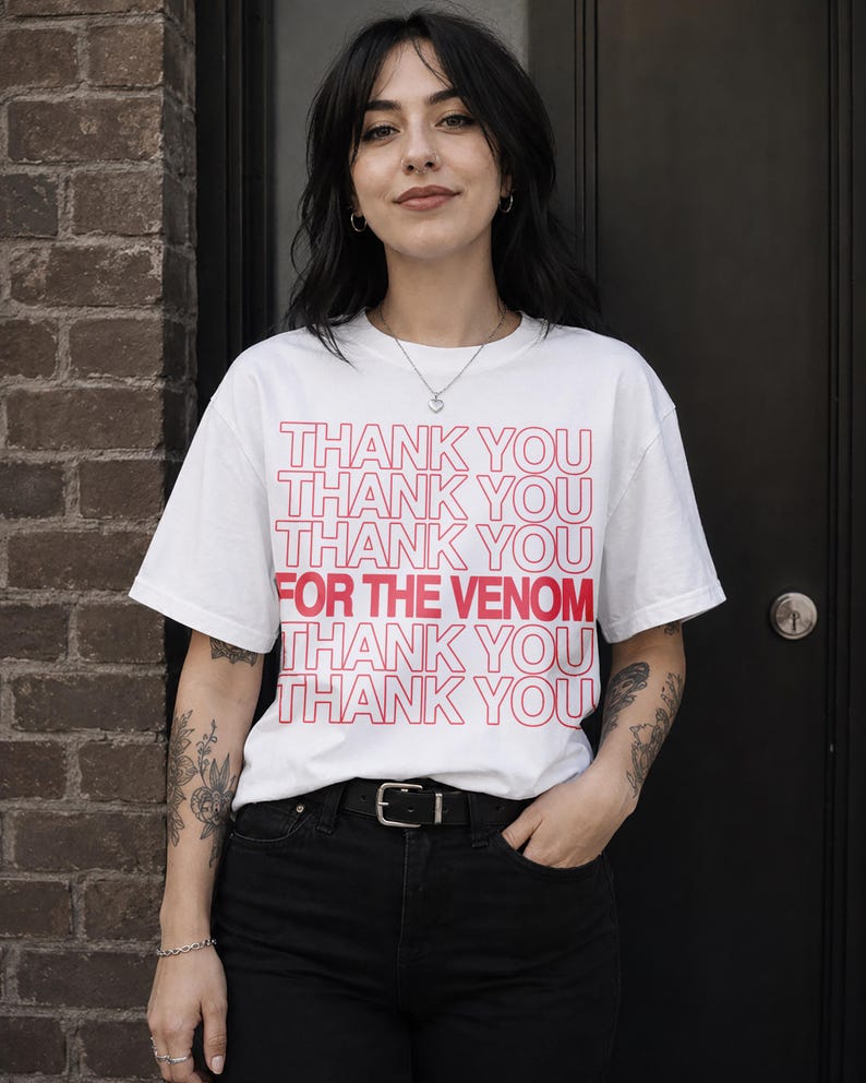 Pu&ograve; includere: T-shirt bianco con la scritta rossa "THANK YOU THANK YOU THANK YOU FOR THE VENOM THANK YOU THANK YOU THANK YOU". La maglietta &egrave; abbinata a jeans neri e una cintura nera.
