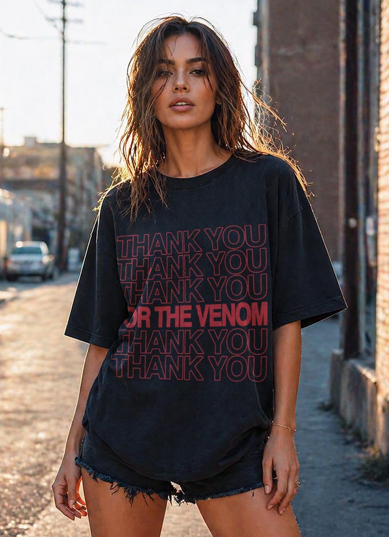 Pu&ograve; includere: T-shirt nero con la scritta "THANK YOU OR THE VENOM" in rosso. La maglietta ha un girocollo e maniche corte. La modella indossa pantaloncini di jeans neri.