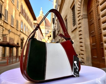 May include: A brown leather handbag with green, white and red panels, resembling the Italian flag. The bag has a short handle and a small tag with the Italian flag on it.