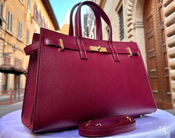 May include: A burgundy leather handbag with gold hardware and a detachable strap. The bag has a structured shape and a top handle.