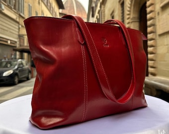 May include: A red leather tote bag with a stitched design and a small logo on the front. The bag is sitting on a white surface.