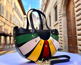May include: A black leather handbag with a colorful, fan-shaped design. The bag features green, pink, yellow, and red stripes, accented with gold-colored studs. It has a top handle and a detachable shoulder strap with a gold chain.