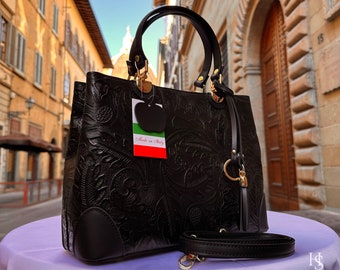 May include: Black leather handbag with an embossed floral design and gold hardware. The bag has a top handle and a detachable shoulder strap. A tag with the text "Made in Italy" is attached to the bag.