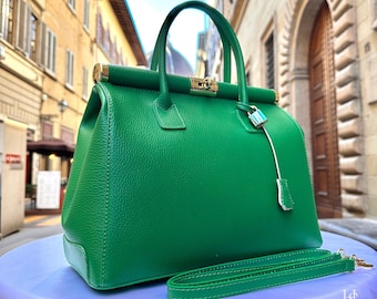 May include: A bright green leather handbag with a gold clasp and a small lock charm. The bag has a top handle and a long adjustable strap. The bag is sitting on a light blue surface.