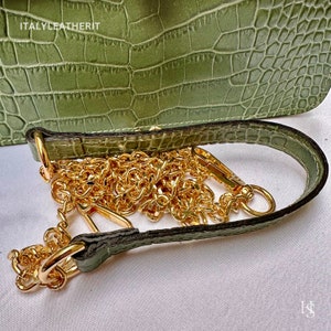 May include: A green crocodile embossed leather handbag with a gold chain strap. The strap is attached to the bag with a gold clasp.