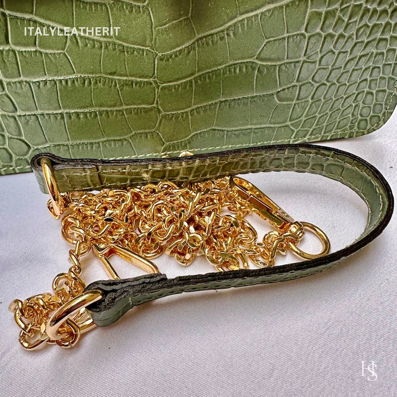 May include: A green crocodile embossed leather handbag with a gold chain strap. The strap is attached to the bag with a gold clasp.