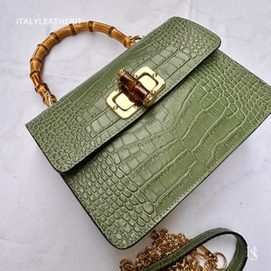 May include: A green crocodile embossed leather handbag with a bamboo top handle and a gold chain strap. The bag has a gold clasp with a bamboo accent.