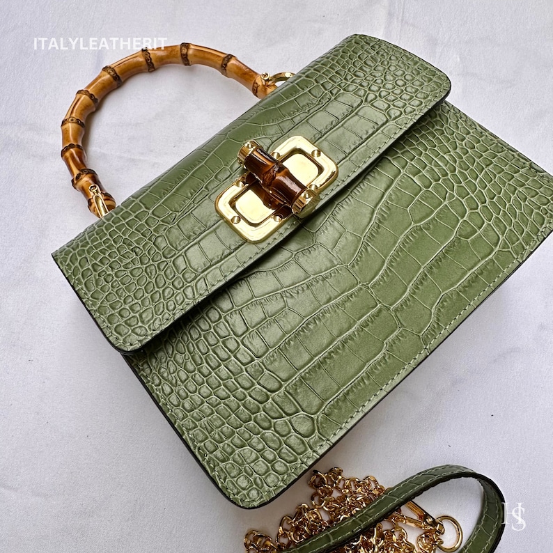 May include: A green crocodile embossed leather handbag with a bamboo top handle and a gold chain strap. The bag has a gold clasp with a bamboo accent.