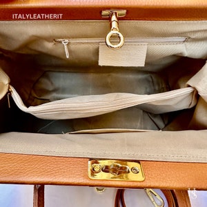 Puede incluir: El interior de una bolsa de m&eacute;dico de cuero marr&oacute;n con un cierre de broche dorado y un bolsillo con cremallera. La bolsa est&aacute; forrada con un tejido beige.