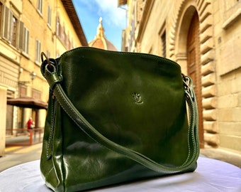 May include: A dark green leather shoulder bag with a gold buckle and a small logo on the front. The bag is sitting on a white surface.