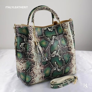 May include: A structured handbag featuring a green, brown and cream snakeskin pattern. The bag has a top handle with gold-tone hardware, a decorative tassel and a detachable shoulder strap. The text ITALYLEATHERIT is visible in the top corner.