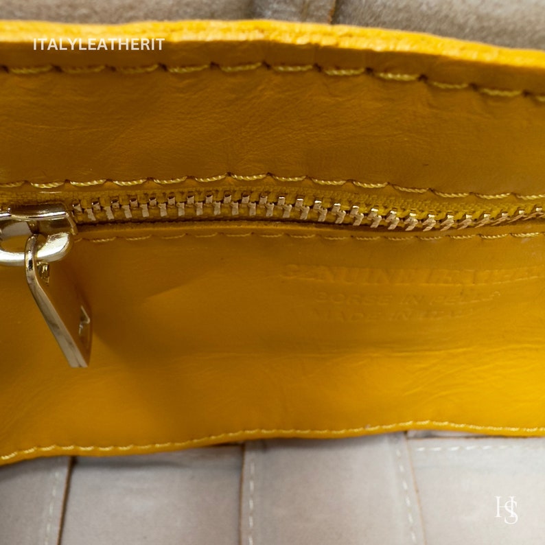 Puede incluir: Primer plano del interior de un bolso de cuero amarillo con cremallera dorada y tirador plateado. Se ven las palabras "GENUINE LEATHER" y "BORSE IN PELLE MADE IN ITALY". Tambi&eacute;n se ven las costuras y la textura del bolso.