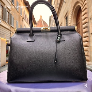 K&ouml;nnte beinhalten: Eine schwarze Ledertasche im Arzt-Stil mit goldenen Beschl&auml;gen und einem kleinen Schloss. Die Tasche hat eine strukturierte Lederoberfl&auml;che und ist geschlossen.