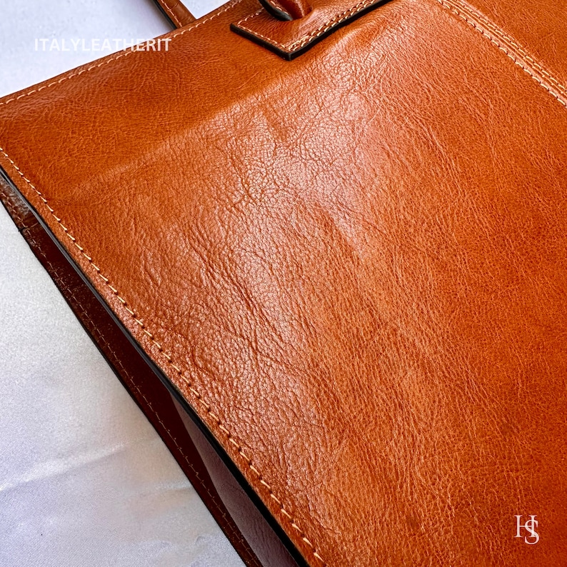 May include: Close-up of a brown leather tote bag with the text "ITALY LEATHERIT" on the front. The bag has a stitched seam around the edge.