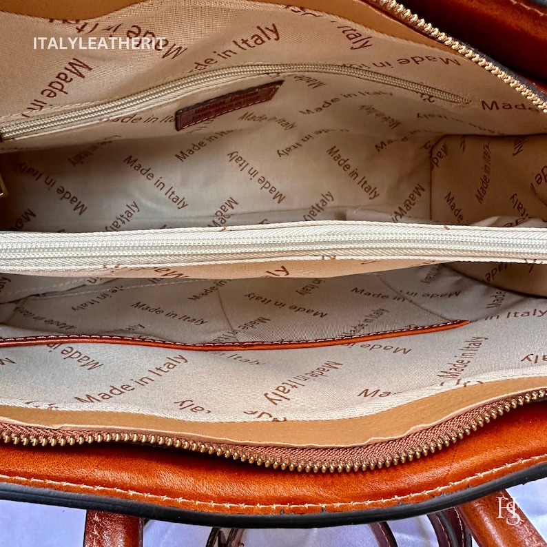 May include: The inside of a brown leather handbag with a zip closure. The lining is beige and has the words "Made in Italy" printed repeatedly.