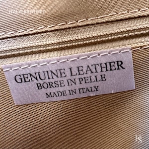 May include: Close-up of a white label with black text that reads "GENUINE LEATHER BORSE IN PELLE MADE IN ITALY".