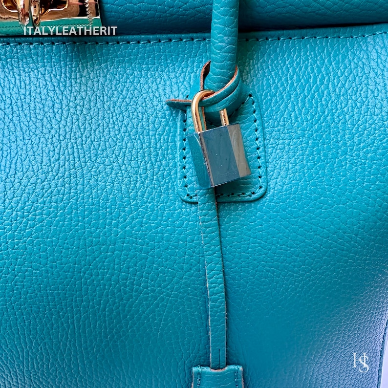 May include: A teal leather handbag with a gold lock and key. The bag has a top handle and a shoulder strap. The text "ITALY LEATHERIT" is visible on the bag.