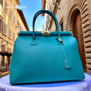 May include: A teal leather handbag with gold hardware and a top handle. The bag has a structured shape and a roomy interior.