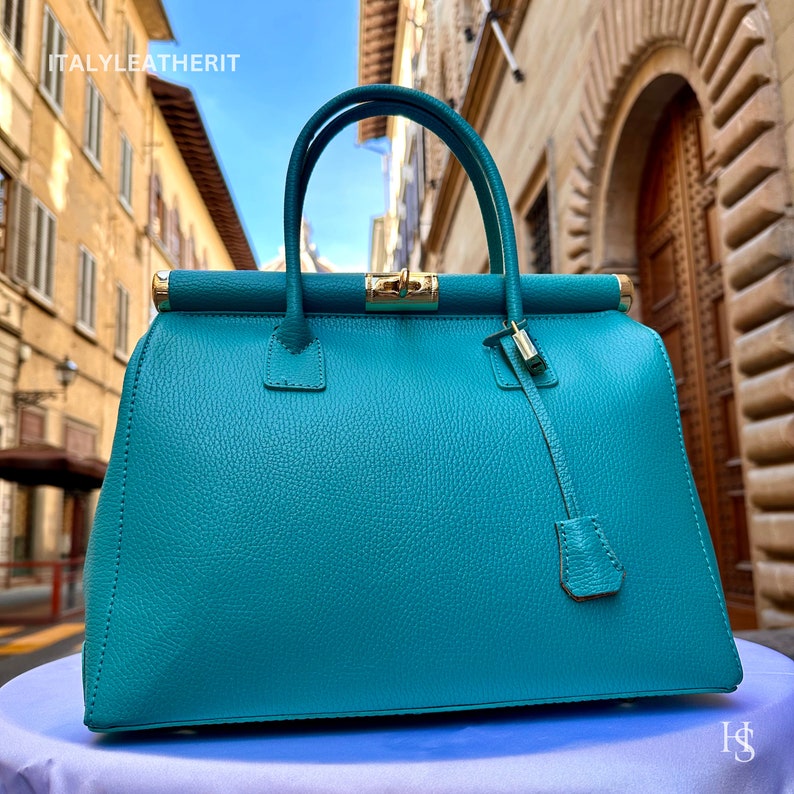 May include: A teal leather handbag with gold hardware and a top handle. The bag has a structured shape and a roomy interior.