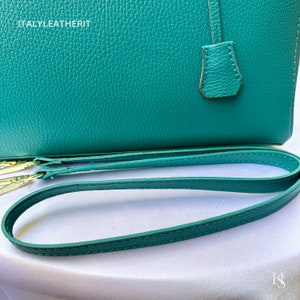 May include: A teal leather handbag with a top handle and a detachable shoulder strap. The strap is teal leather with gold hardware. The bag has the text "ITALY LEATHERIT" embossed on the front.