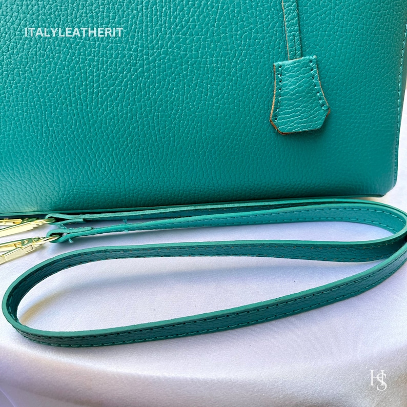 May include: A teal leather handbag with a top handle and a detachable shoulder strap. The strap is teal leather with gold hardware. The bag has the text "ITALY LEATHERIT" embossed on the front.