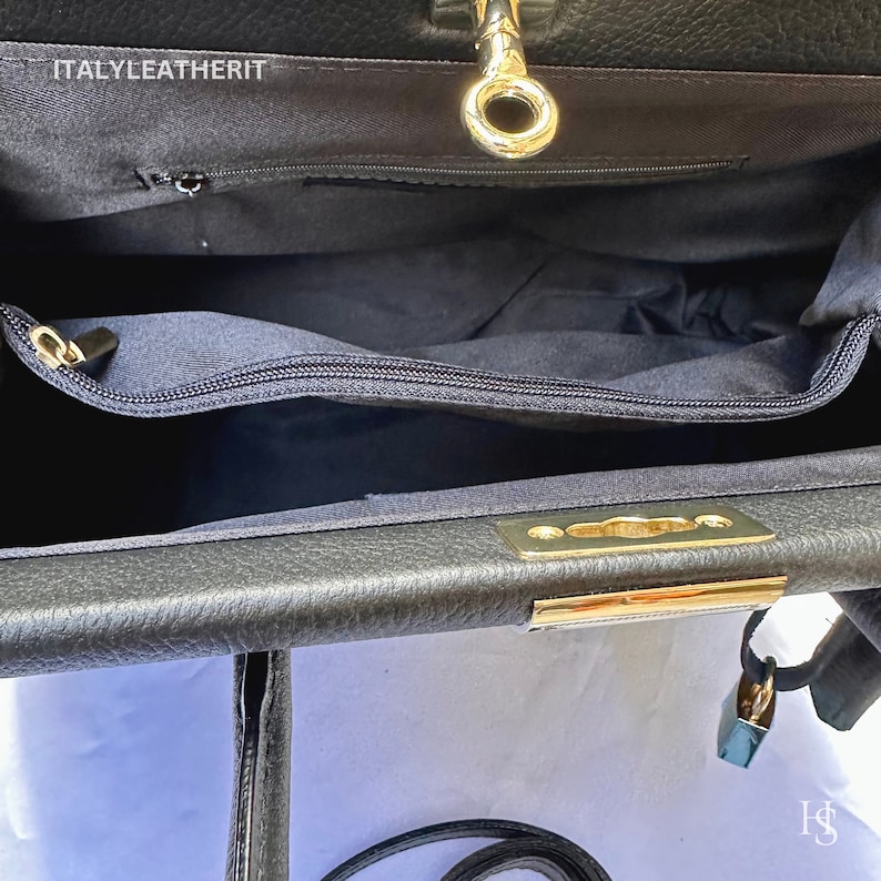 K&ouml;nnte beinhalten: Schwarze Ledertasche mit goldenem Schloss und Schl&uuml;sselloch. Die Tasche hat eine Rei&szlig;verschlusstasche innen und einen goldenen Metallverschluss.