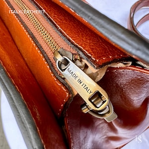 May include: Close-up of a brown leather bag with a zipper and a metal tag that reads "Made in Italy".