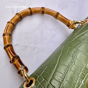 May include: A green crocodile embossed leather handbag with a bamboo top handle. The handle is secured with gold hardware.