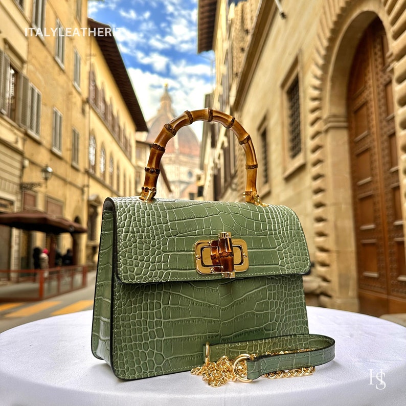 May include: A green crocodile embossed leather handbag with a bamboo top handle and a gold chain strap. The bag has a gold clasp with a bamboo design.