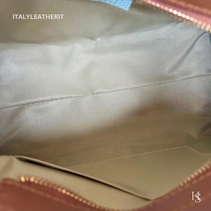 Puede incluir: Vista interior de un bolso de mano de cuero marr&oacute;n con forro de tela beige claro. El bolso tiene un cierre de cremallera y un peque&ntilde;o bolsillo. El texto "ITALYLEATHERIT" es visible.