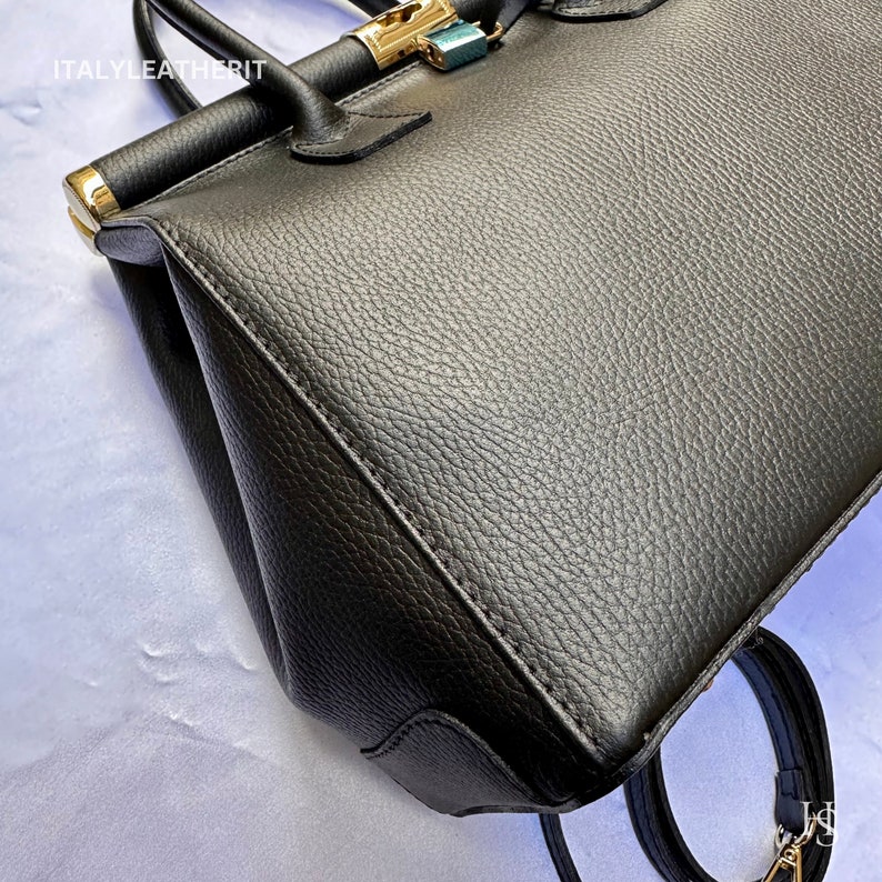 K&ouml;nnte beinhalten: Schwarze Ledertasche mit goldenen Beschl&auml;gen und einer strukturierten Oberfl&auml;che. Die Tasche hat einen oberen Henkel und einen Schultergurt. Der Markenname "ITALY LEATHERIT" ist auf der Vorderseite der Tasche sichtbar.