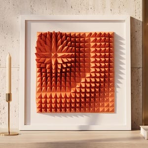 Könnte beinhalten: Ein quadratisches Wandkunstwerk in einem weißen Rahmen mit einer dreidimensionalen orangefarbenen Platte, die ein sich wiederholendes geometrisches Pyramidenmuster aufweist. Das Design enthält eine sternförmige Anordnung.