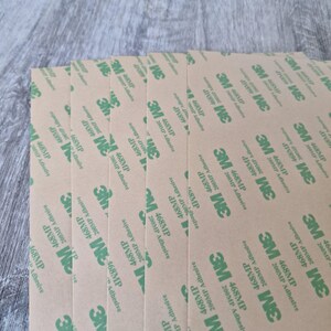 May include: A stack of brown adhesive sheets with green 3M branding and the text "468MP 200MP Adhesive" repeated on each sheet.
