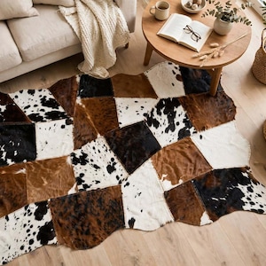 Peut inclure: Un tapis rectangulaire composé de pièces de peau de vache cousues ensemble dans des tons variés de brun, noir et blanc. Le tapis présente un motif en patchwork avec des formes et des textures irrégulières, mettant en valeur les motifs naturels.