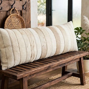May include: A long rectangular lumbar pillow featuring a vertical striped pattern in alternating shades of cream, beige, and light brown. The pillow has a textured surface and is positioned horizontally on a dark brown wooden bench seat.