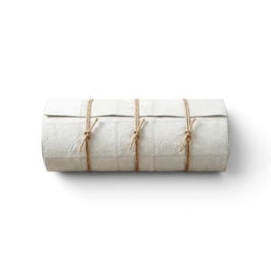 May include: A cylindrical roll of off-white, textured material featuring a grid-like pattern of stitched seams. The roll is secured by three thin, brown twine cords tied in simple knots at regular intervals along its length.