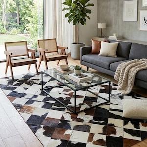 Può includere: Un tappeto rettangolare caratterizzato da un design patchwork di quadrati in pelle bovina nei colori nero, bianco e marrone. Il tappeto è disposto con un motivo a rombi ed è posizionato sotto un tavolino rettangolare in vetro con telaio in metallo nero.