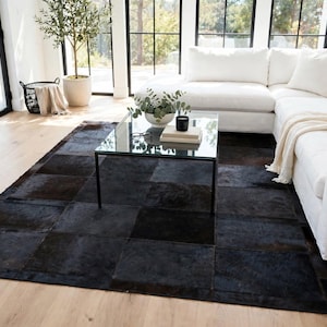 May include: A large rectangular area rug constructed from stitched square panels of dark brown and black cowhide leather. The rug features a patchwork design with a natural hair-on-hide texture, displaying varied deep tones and a smooth finish.